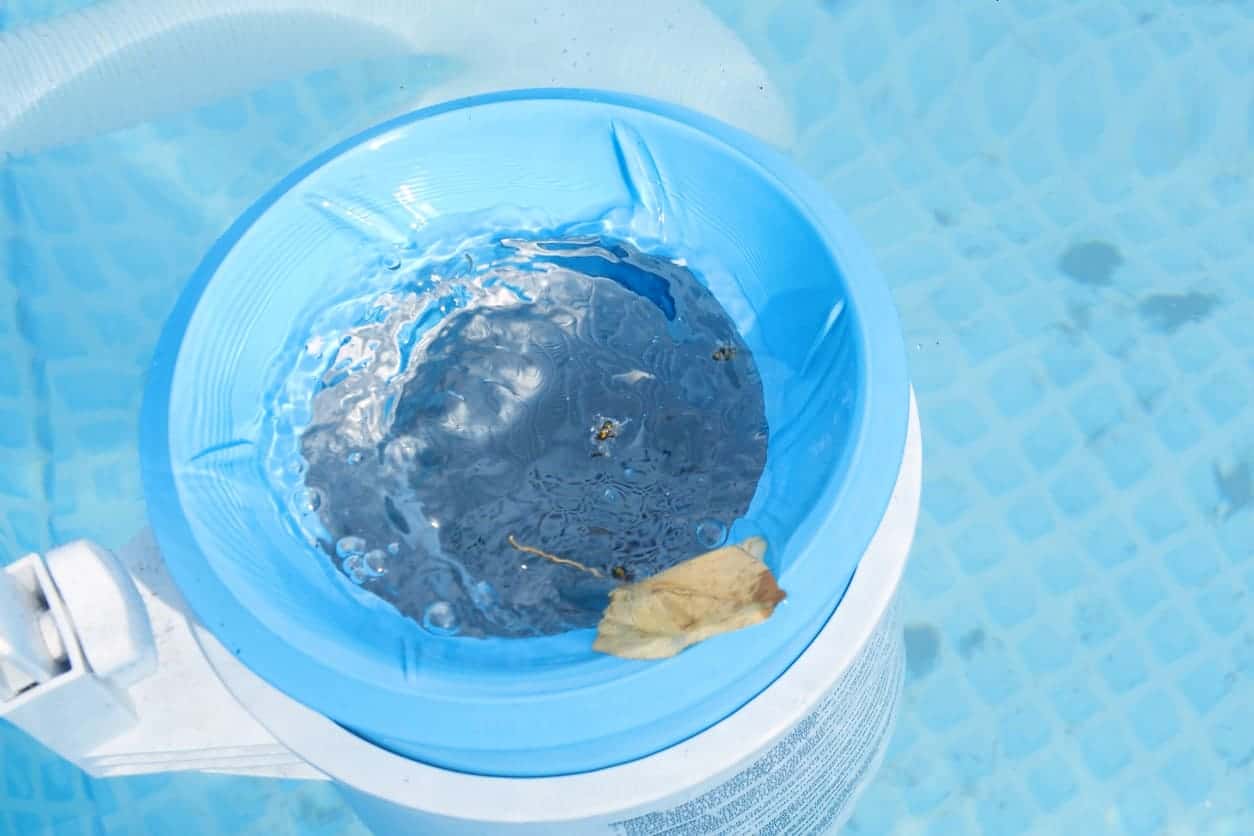 A Patriot Pool and Spa skimmer filled with water floats in the light blue, tiled swimming pool, effortlessly catching small leaves and debris.